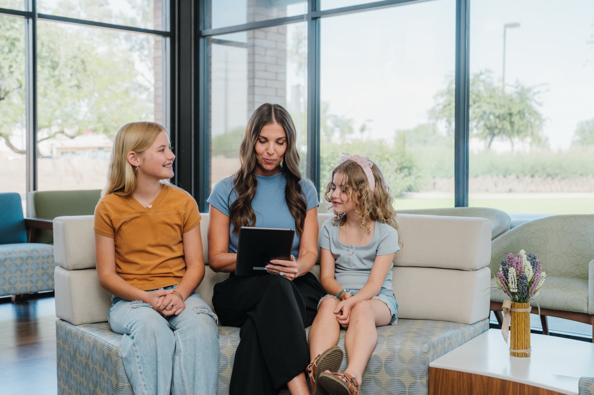 A mother and her two daughters looking at the patient portal on a tablet in a waiting room